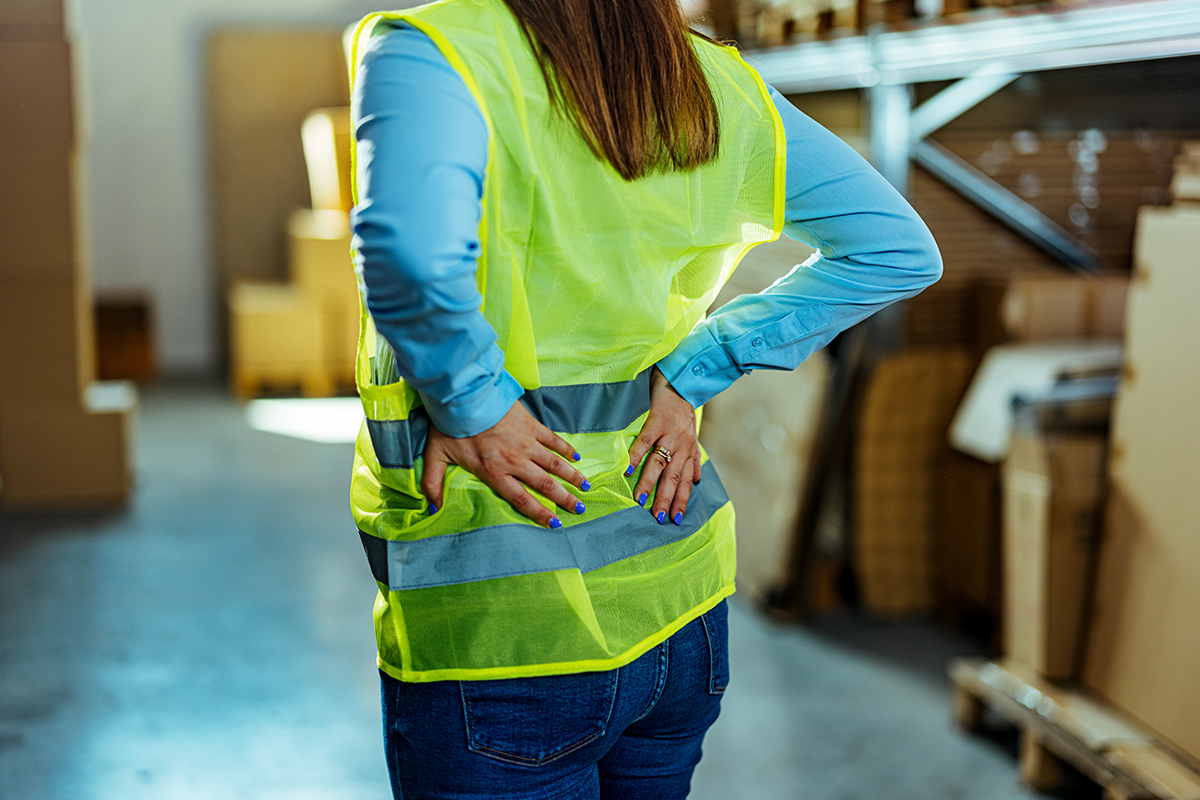 a woman in a warehouse holding her lower back after needing a chiropractic treatment in Fort Worth.