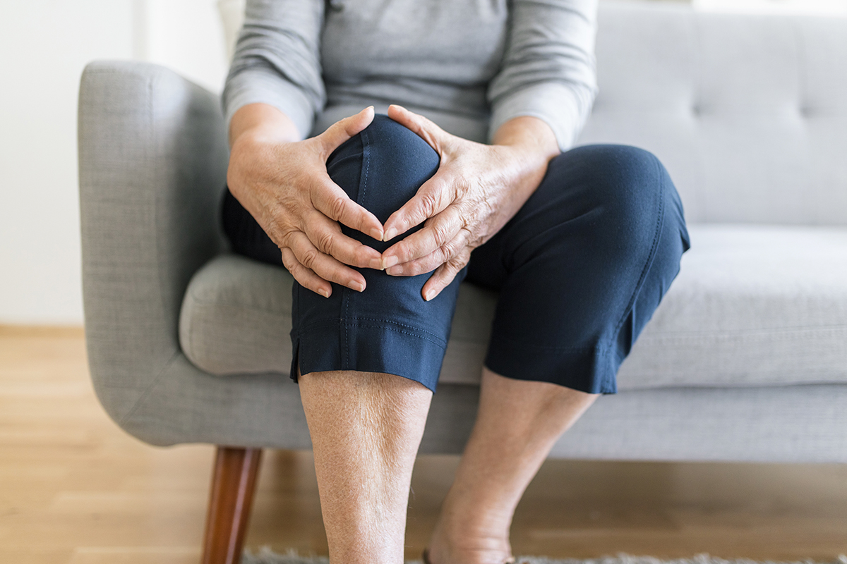 a woman sitting on a couch holding her knee before getting PRP therapy in Fort Worth.
